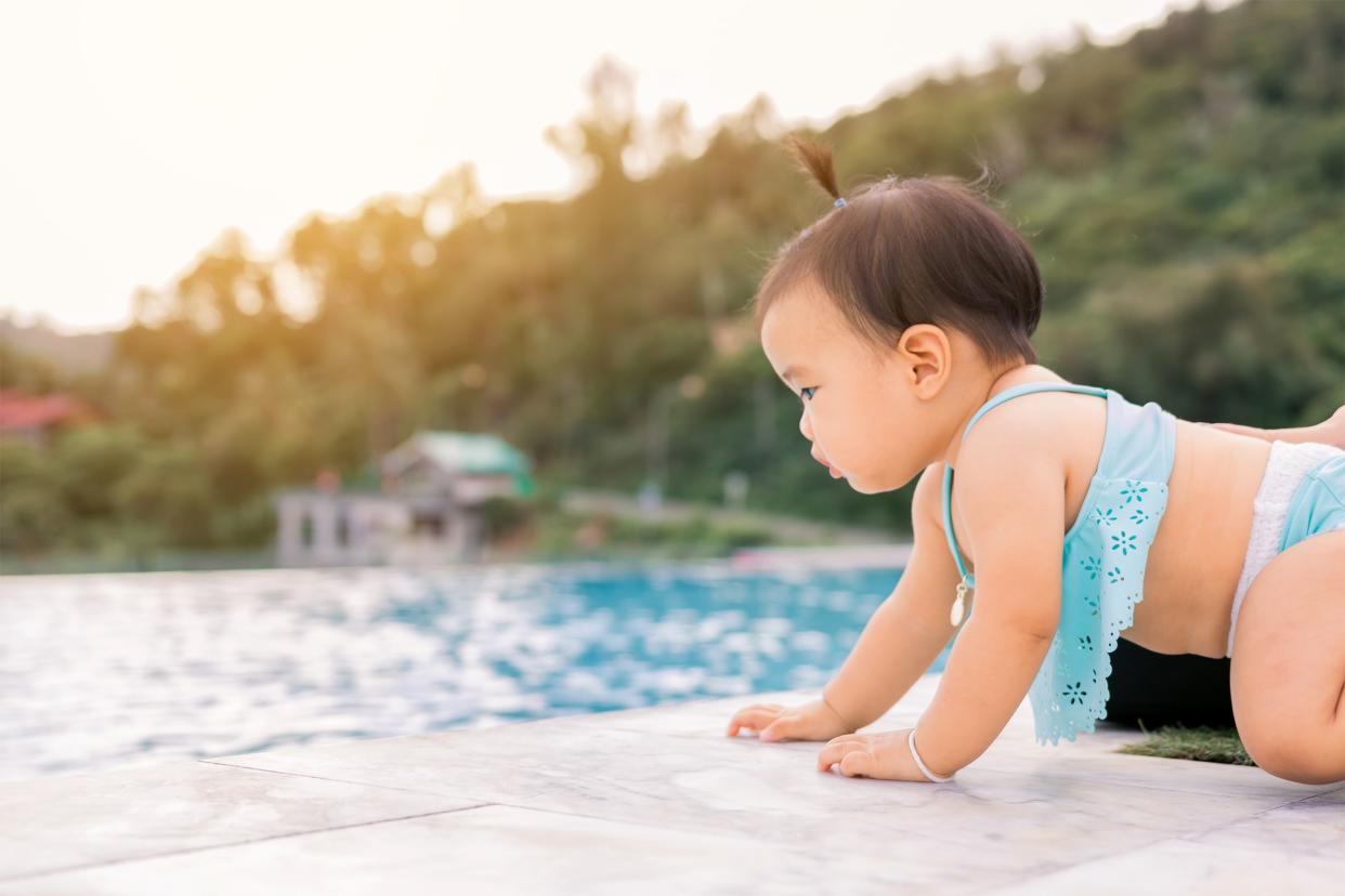 Female infant approaching the edge into the water of an in-ground swimming pool, alone with danger with blurred background