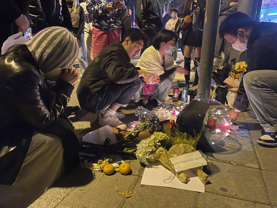 Residents mourn for the victims of a recent deadly fire at a residential building in Urumqi city at a road sign of the Middle Wulumuqi Road or Middle Urumqi Rd in Shanghai, China Saturday, Nov. 26, 2022. Protests against China's restrictive COVID-19 measures appeared to roil in a number of cities Saturday night, in displays of public defiance fanned by anger over a deadly fire in the western Xinjiang region. (Chinatopix Via AP)