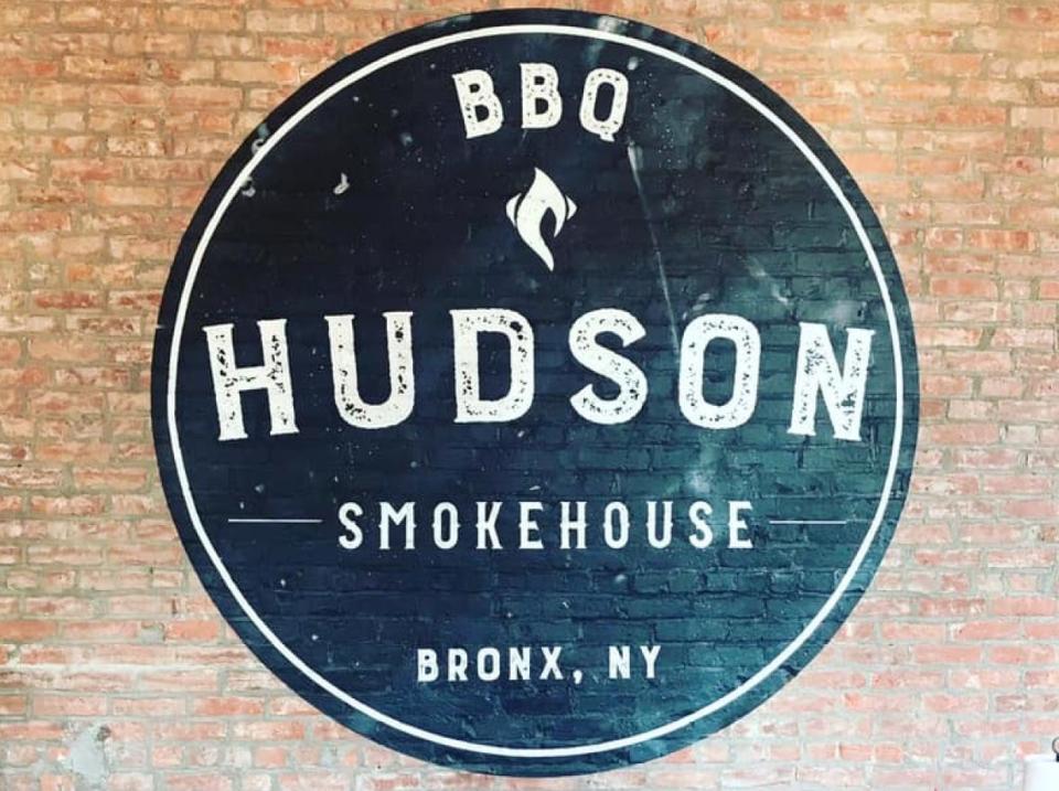 A black sign on a brick wall for Hudson Smokehouse BBQ.
