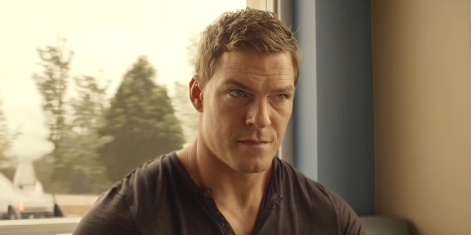 alan ritchson as jack reacher in amazon series reacher, sitting in a cafe wearing a black tshirt