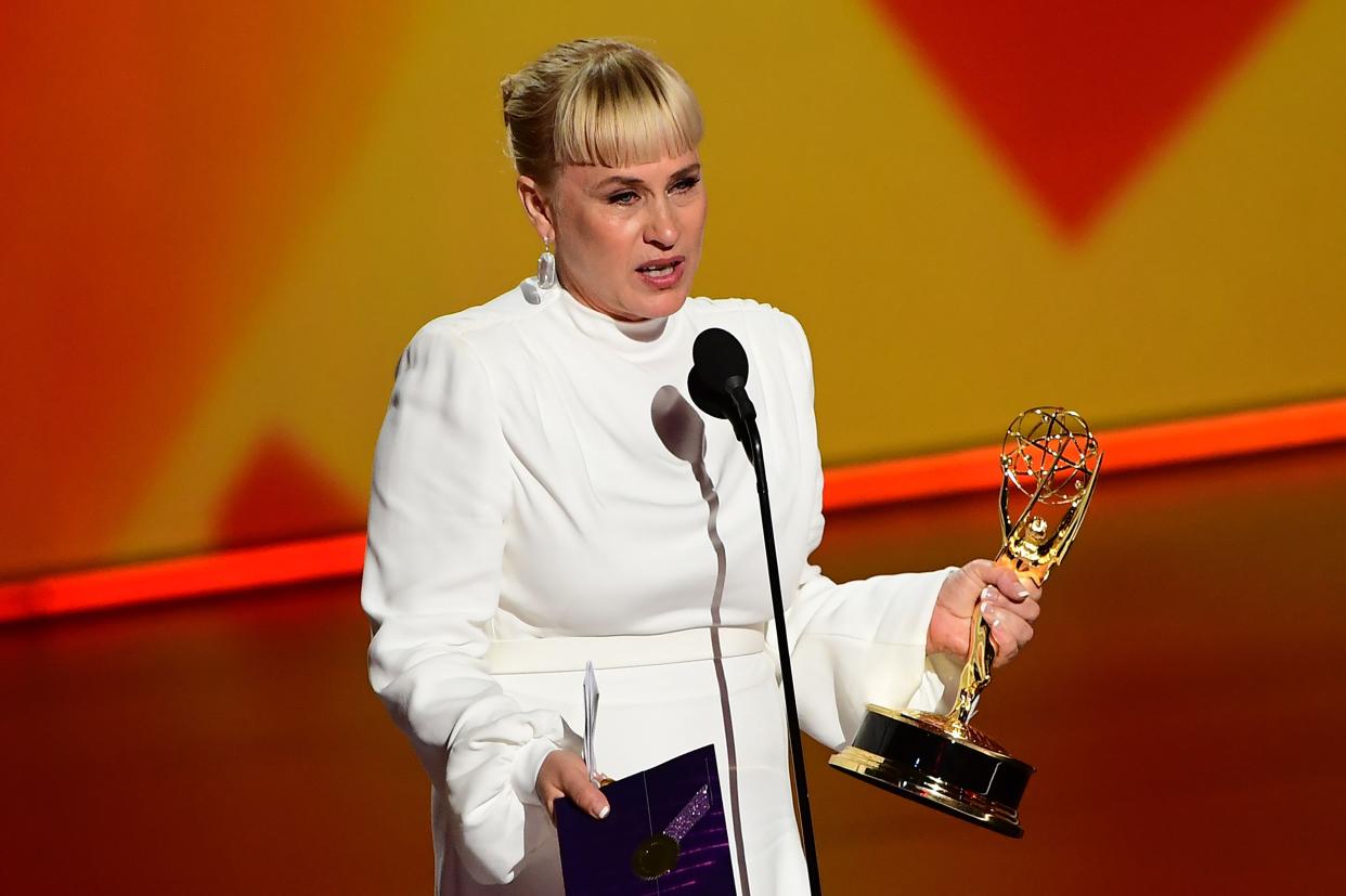 Patrcia Arquette stands on stage talking into a microphone and holding an Emmy Award