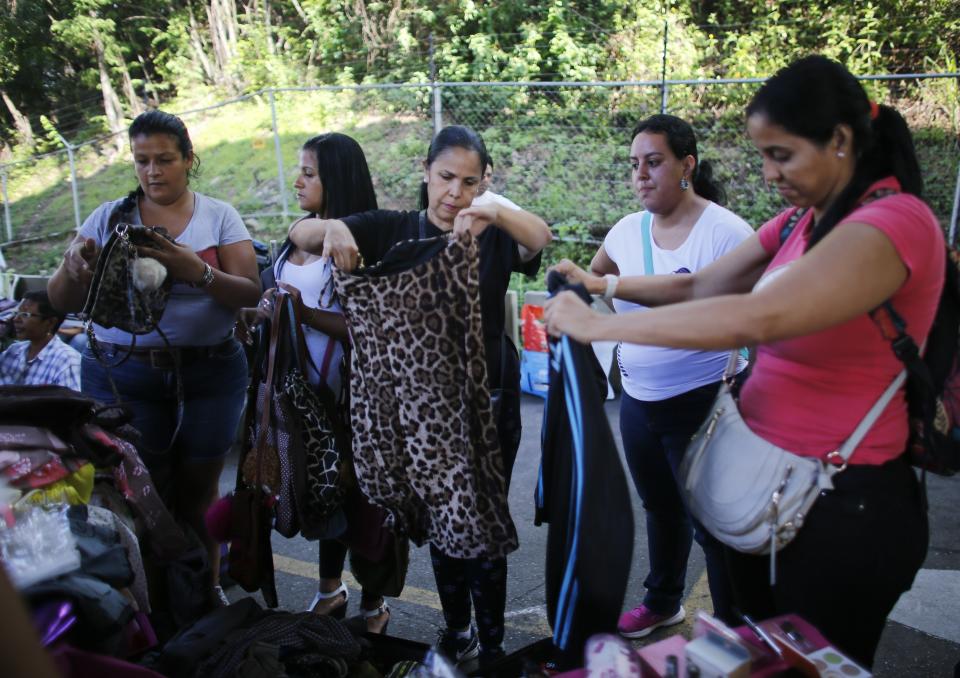 In this Nov. 3, 2019 photo, women look through used clothing at a secondhand market in Caracas, Venezuela. Some of the secondhand street markets pop up on Sundays or get organized through social media. Sellers bank on peddling personal items like clothes and household items to finance a new life abroad. (AP Photo/Ariana Cubillos)