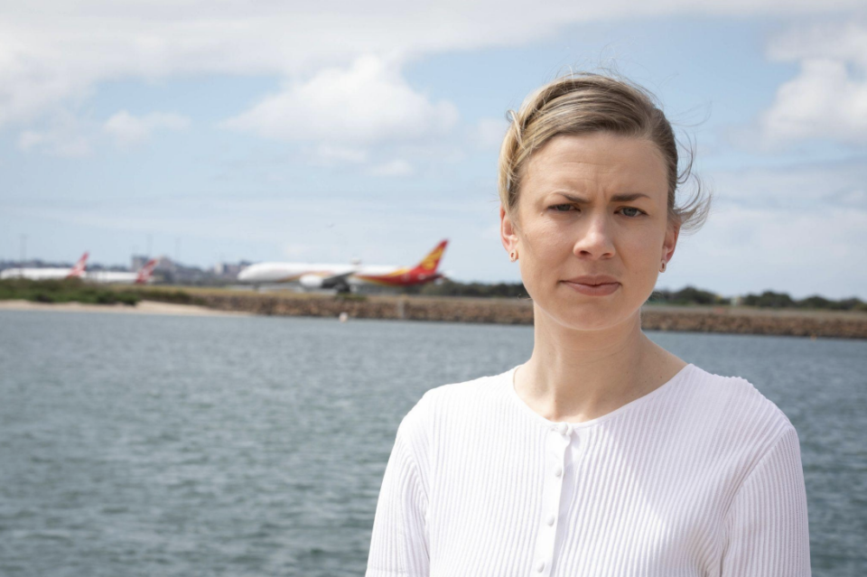 Woman looks at camera with water and plane in the background. 