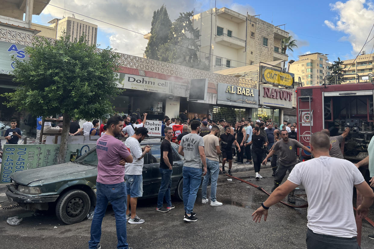 Smoke rises from a mobile phone shop in Sidon, Lebanon, as people gather in the street.