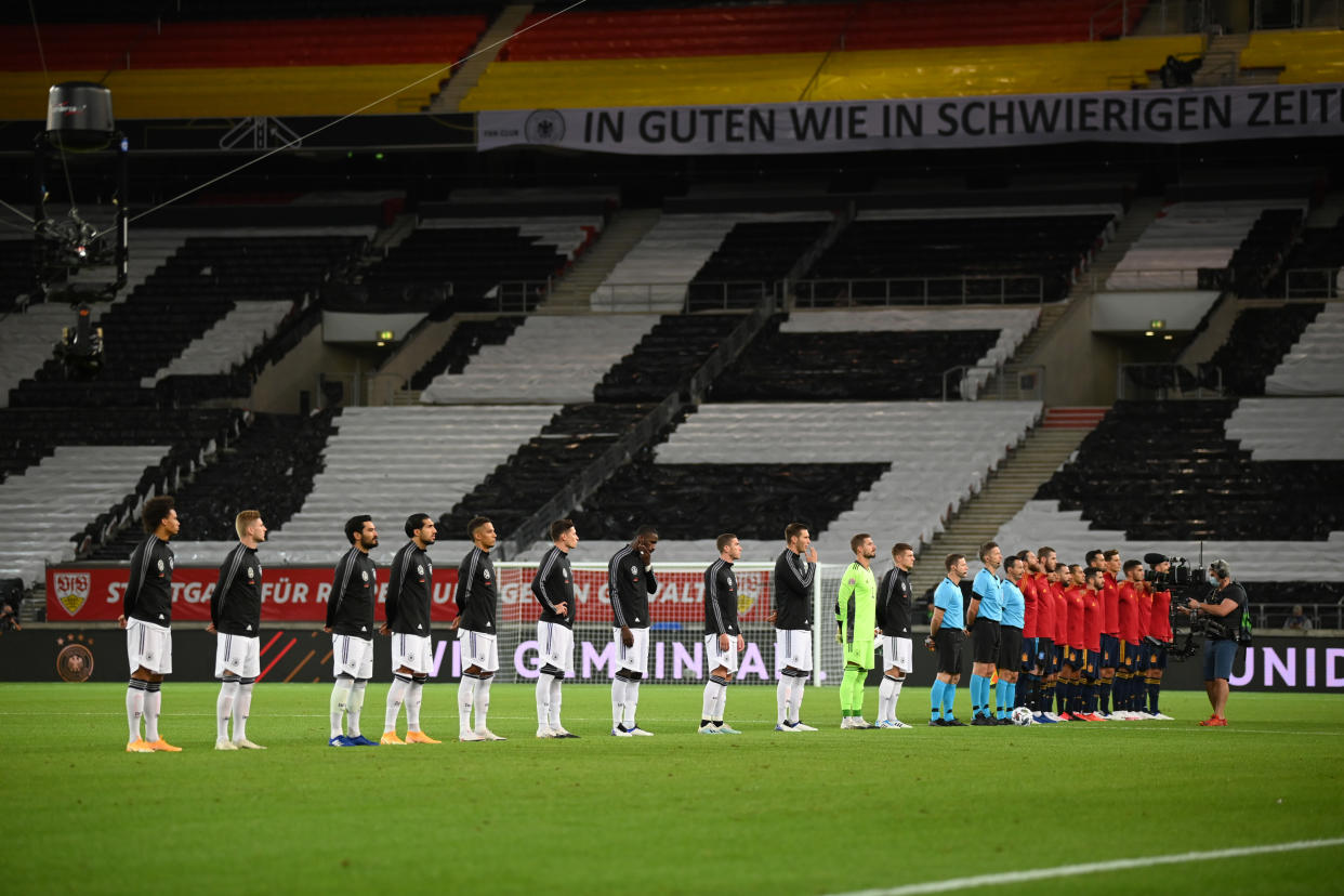 Jugadores alemanes y españoles alineados ante la grada del estadio vacío de Stuttgart.