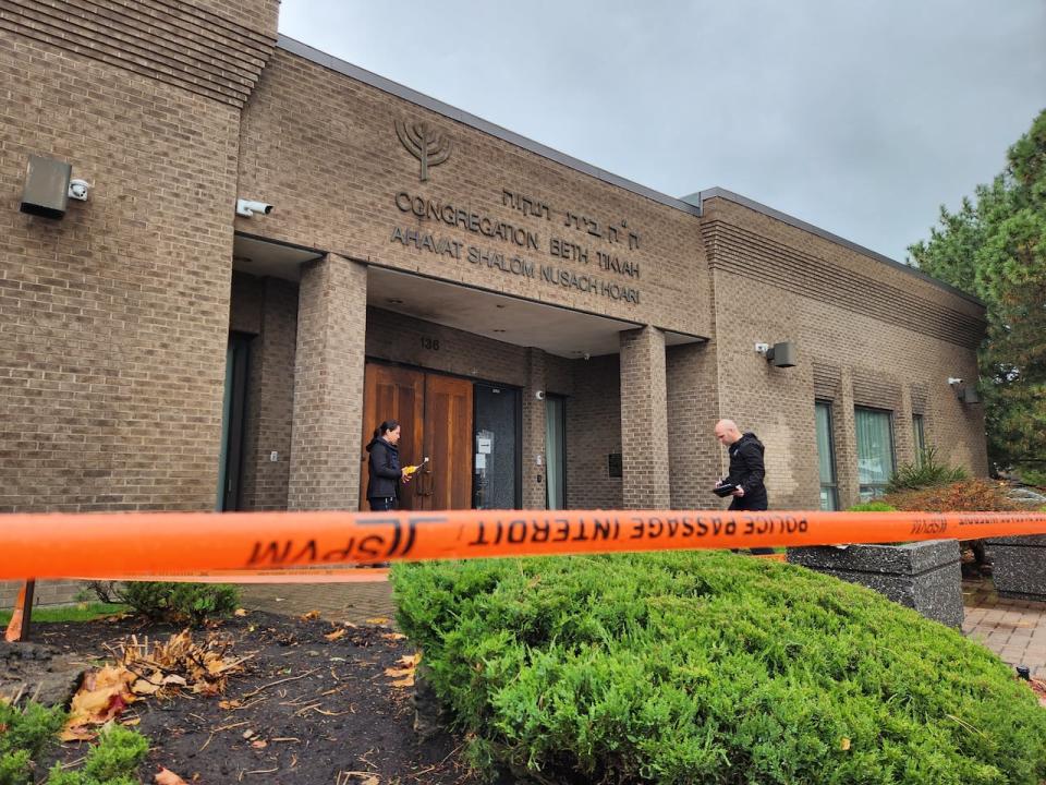 Police investigators examine the exterior of a synagogue in Dollard-des-Ormeaux, Que., where an incendiary device was ignited overnight Monday. 