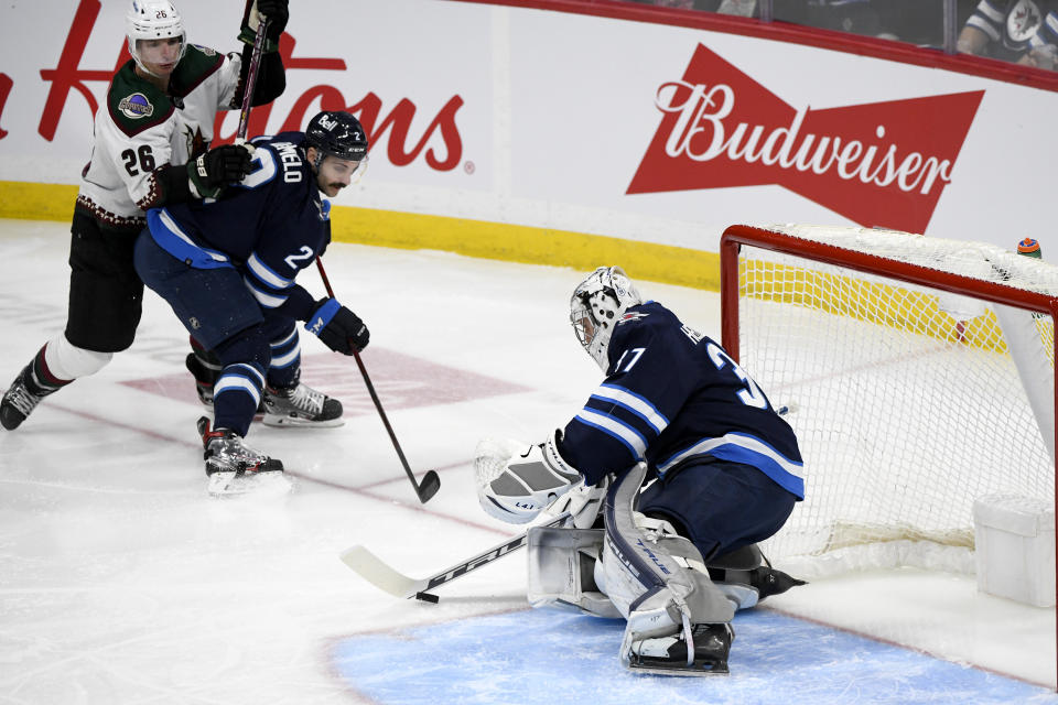 Winnipeg Jets goaltender Connor Hellebuyck (37) makes a save against Arizona Coyotes' Antoine Roussel (26) as Jets' Dylan DeMelo (2) defends during the first period of NHL hockey game action in Winnipeg, Manitoba, Monday, Nov. 29, 2021. (Fred Greenslade/The Canadian Press via AP)