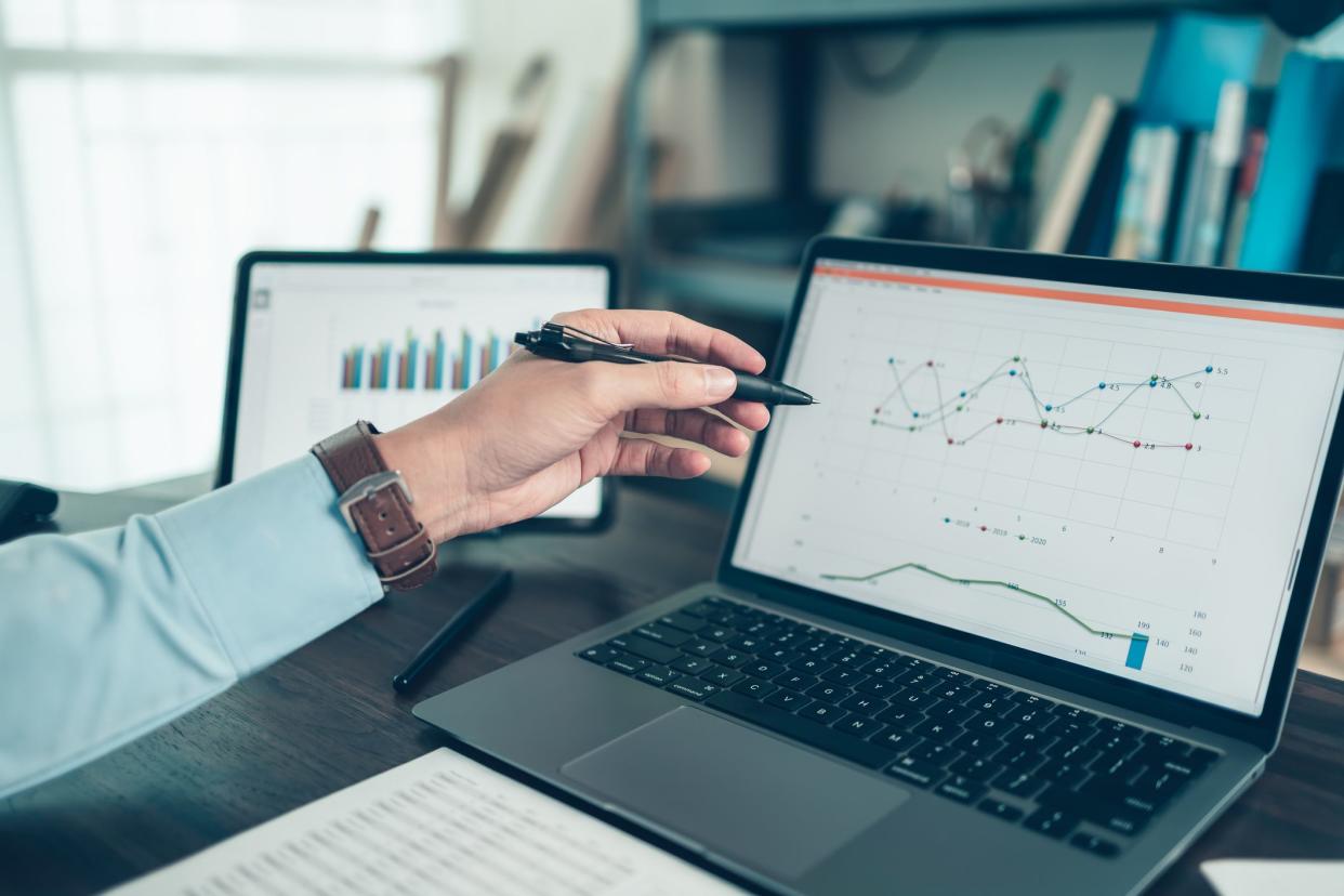 Business man hold stylus pen and pointing to laptop at office  with document report, graph, financial report on screen.