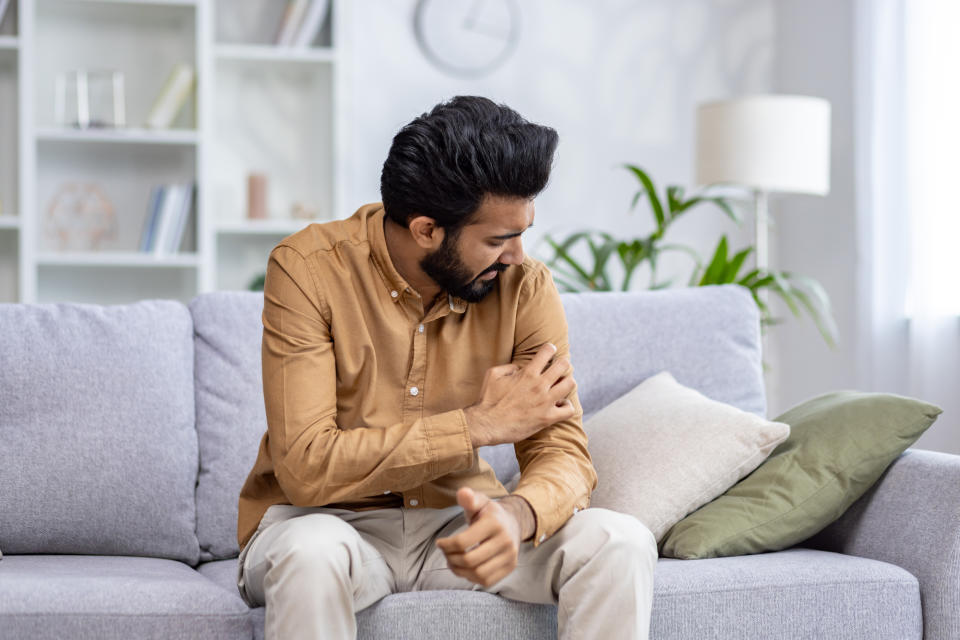 Man sitting on couch appearing to be in pain as he holds his upper arm