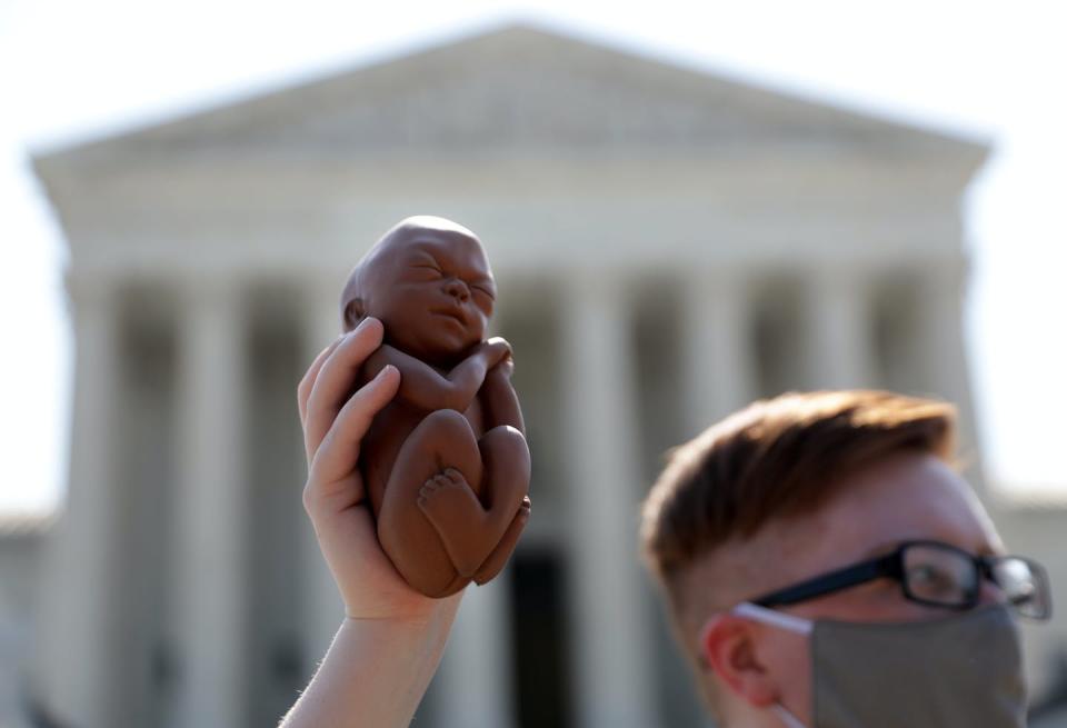 A young man in front of the US Supreme Court holds up a model of a fetus a bit bigger than his hand.