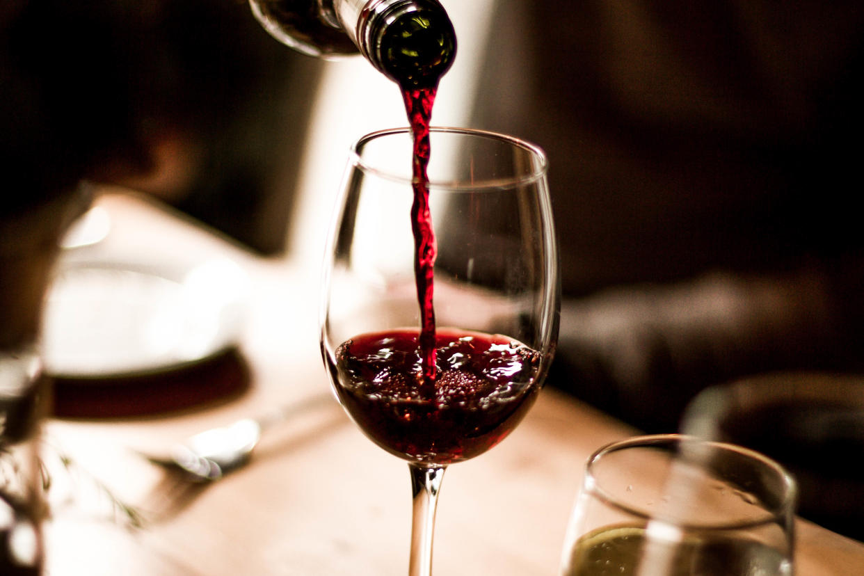 Red wine being poured into a stem glass at the table.