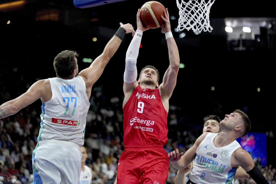 Mateusz Ponitka, de la selección de Polonia, al centro, busca la canasta frente al astro Luka Doncic, del equipo de Eslovenia (77), en el último cuarto del partido que ganaron los polacos para avanzar a las semifinales de torneo Eurobasquet, en Berlín Alemania, el miércoles 14 de septiembre de 2022. (AP Foto/Michael Sohn)