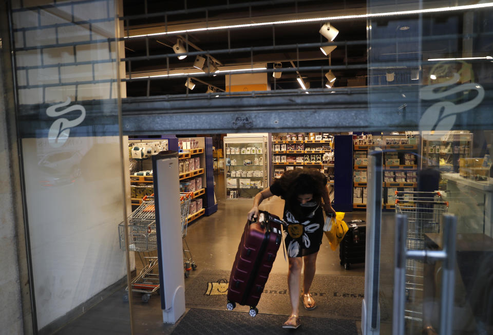 A customer carries luggage out of an international fashion and homeware retailer that will temporarily shut down from Friday in the face of an increasingly volatile currency market and their inability to set prices while the Lebanese pound plunges against the dollar, in Beirut, Lebanon, Thursday July 2, 2020. Later in the day, owners of the businesses rallied in central Beirut to denounce the government's inability to handle a deepening economic and financial crisis, and urging others to join them after the Lebanese pound recorded a new low Thursday, selling at nearly 10,000 for a dollar and maintaining the downward slide that saw the national currency lose about 85% of its value over the past months. (AP Photo/Hussein Malla)