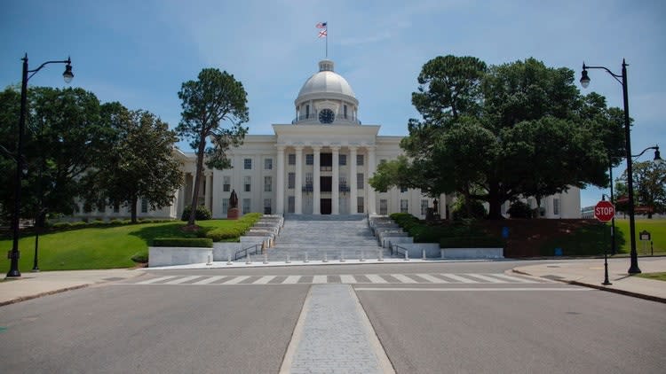 A white building with a dome and a flag on top with Alabama State Capitol in the background Description automatically generated