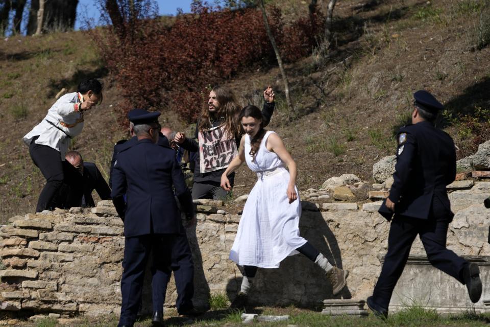 Police officers run to detain protesters displaying a Tibetan flag and a banner disrupting the lighting of the Olympic flame at Ancient Olympia site, birthplace of the ancient Olympics in southwestern Greece, Monday, Oct. 18, 2021. The flame will be transported by torch relay to Beijing, China, which will host the Feb. 4-20, 2022 Winter Olympics. (AP Photo/Thanassis Stavrakis)