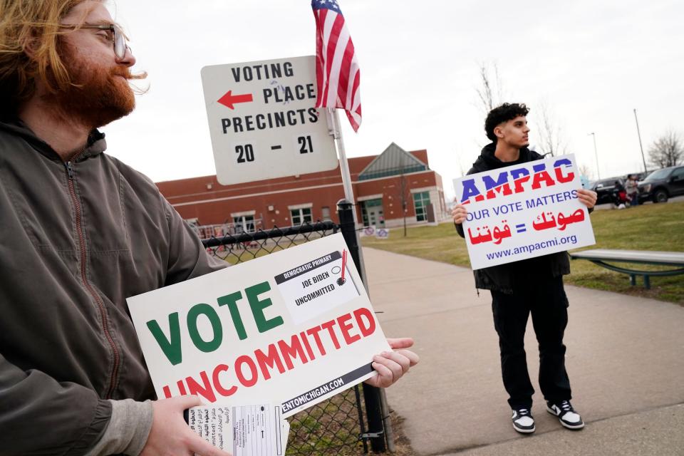 Eric Suter-Bull of Washington, D.C., left, holds a "Vote Uncommited" as a protest vote against Joe Biden as Mohamed Fateeh, 18, holds a AMPAC sign for potential voters to see as they enter Salina Intermediate School in Dearborn to cast their votes in the presidential primary onTuesday, Feb. 27, 2024.