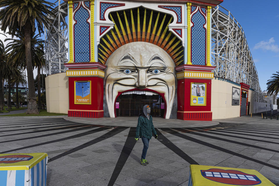 A man wearing a mask walks past Luna Park in the suburb of St Kilda during lockdown in Melbourne, Australia, Wednesday, Aug. 5, 2020. People are allowed to exercise for one hour a day within a 5-kilometer radius of their house. Victoria state, Australia's coronavirus hot spot, announced on Monday that businesses will be closed and scaled down in a bid to curb the spread of the virus. (AP Photo/Asanka Brendon Ratnayake)