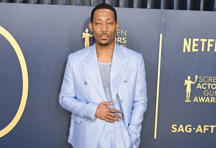 Jonathan Majors on the red carpet wearing a glimmering blue suit with a patterned shirt and white shoes