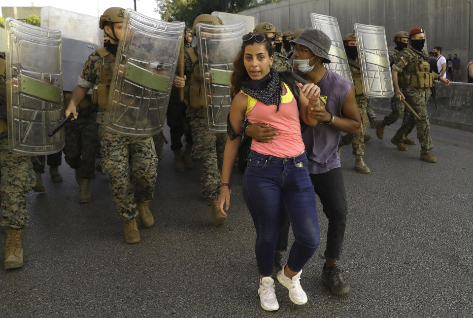 An anti-government protester protects her friend from the Lebanese soldiers, during a protest against the Lebanese President Michel Aoun near the presidential palace, in Baabda east of Beirut, Lebanon, Saturday, Sept. 12, 2020. Lebanese soldiers on Saturday fired rubber bullets and live rounds in the air to disperse hundreds of protesters trying to march to the presidential palace during an anti-government demonstration. (AP Photo/Bilal Hussein)