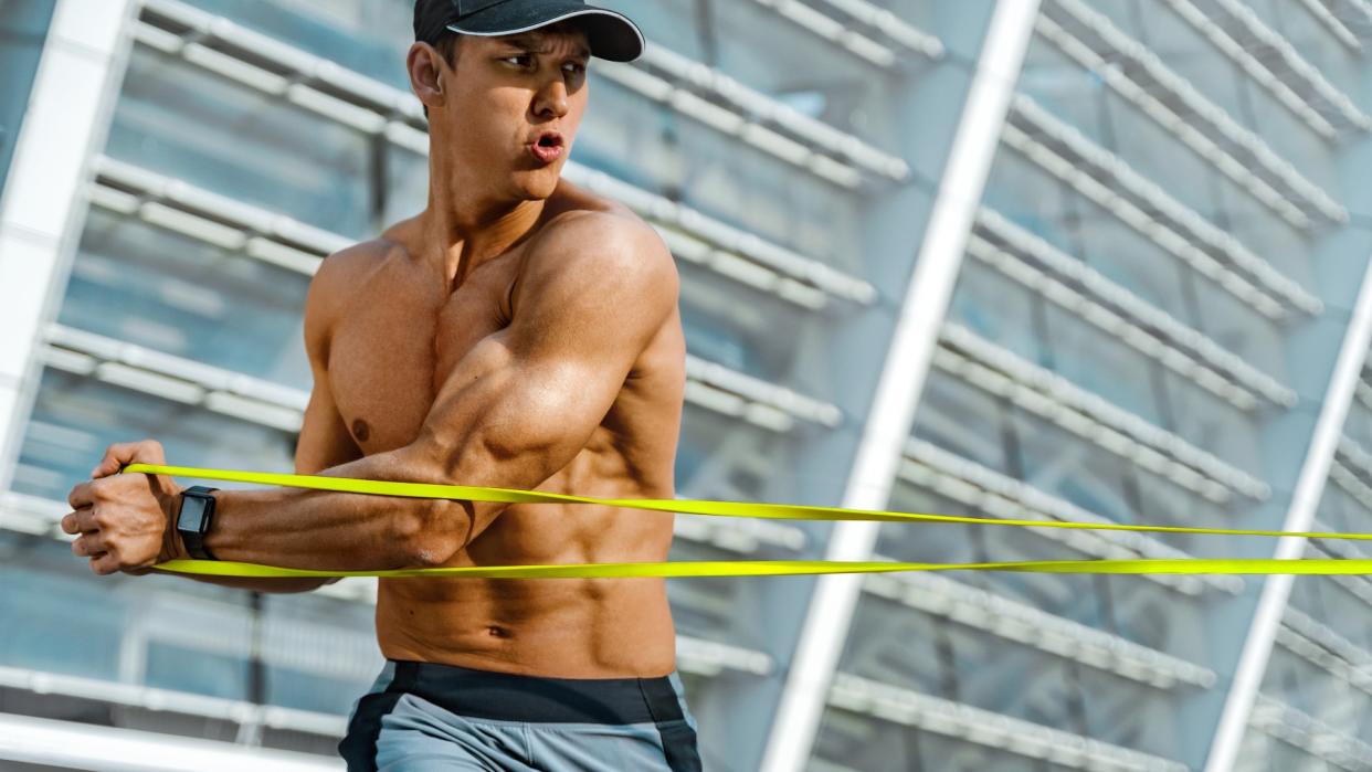  Man outside pulling a resistance band to one side during a twist exercise . 