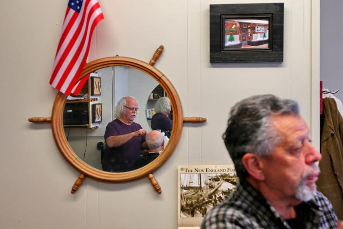 James Lopes waits for his turn, as Manny Medeiros is reflected in the mirror hanging on the wall at Not Your Father's Moustache in downtown New Bedford.  Mr. Medeiros is set to retire at the end of next month.