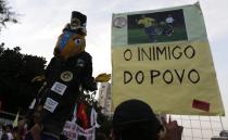 A demonstrator holds a banner with a picture of Brazil's former soccer player and member of the Local Organizing Committee Ronaldo (R) and another one holds a doll in the likeness of 2014 World Cup mascot Fuleco during a protest against the 2014 World Cup in Rio de Janeiro May 15, 2014. Brazilians opposed to the World Cup and the public funds spent on the construction of stadiums called for a day of protests around the country. The banner reads "Enemy of People". REUTERS/Ricardo Moraes (BRAZIL - Tags: SPORT SOCCER WORLD CUP CIVIL UNREST)