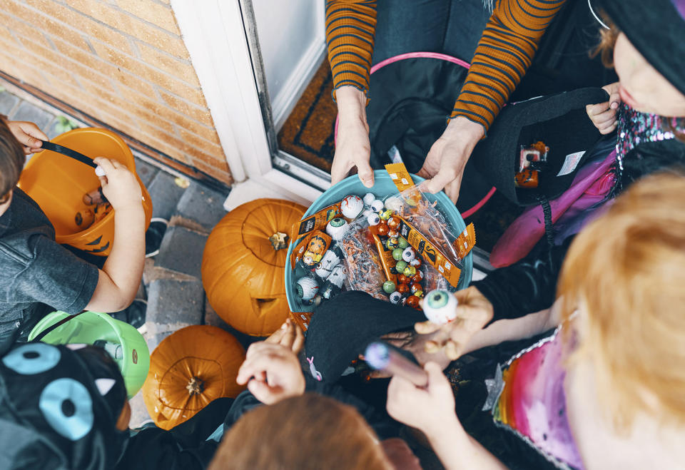 Overhead view  of a group of children at a front door taking sweets from a bowl at Halloween. (Wholly Owned ISUnited Kingdom / Getty Images/Image Source)