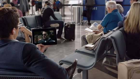 A person sitting in an airport watching a video on a tablet.