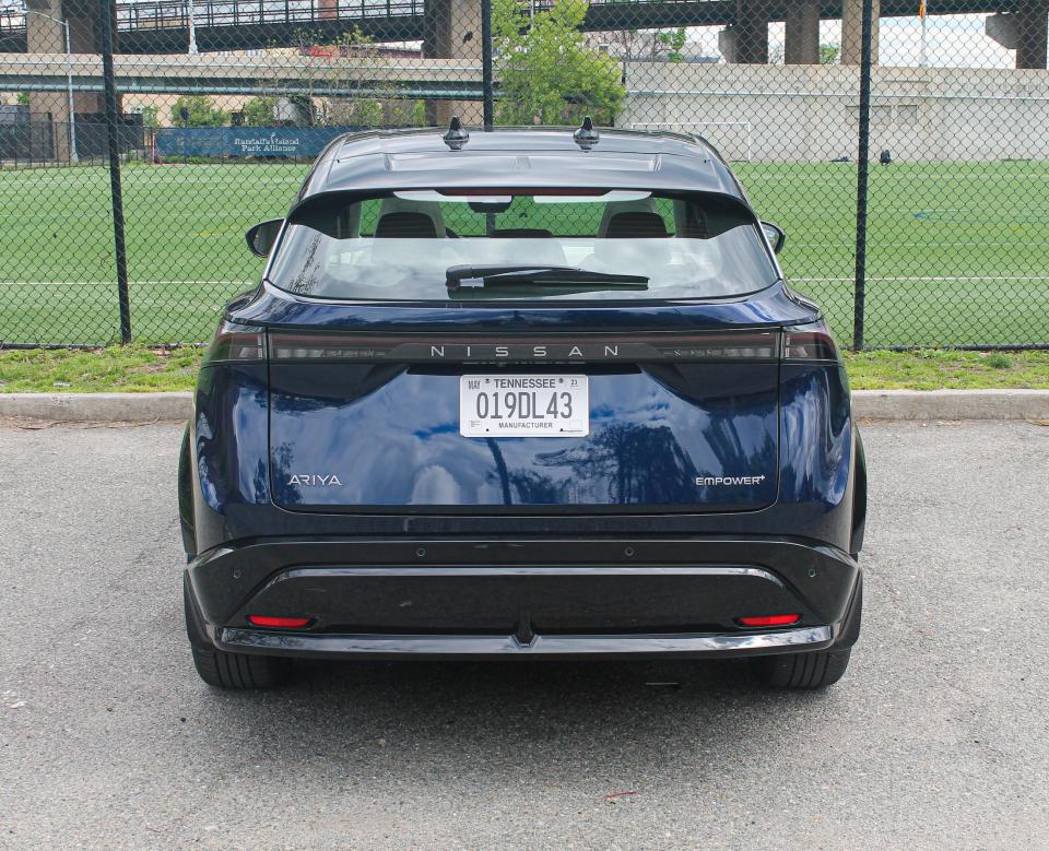 A blue 2023 Nissan Ariya electric SUV seen from the rear, with a grass field in the background.