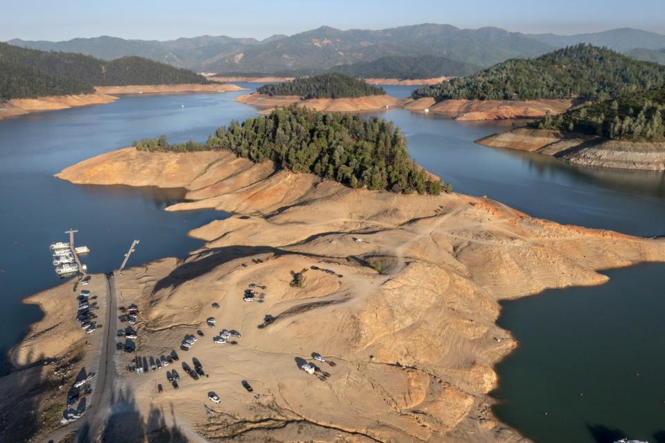 Evergreen trees stand marooned well above the water level on islands and the shore of a large but receding lake