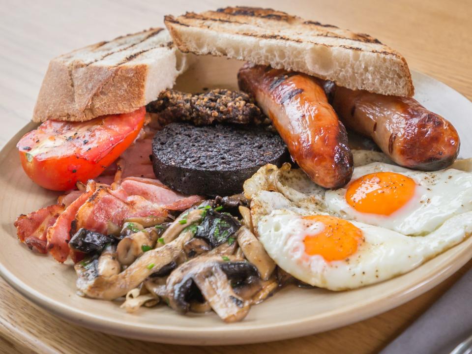 toast, black pudidng, a fried egg, mushrooms, a tomato slice, sausage and bacon on a plate