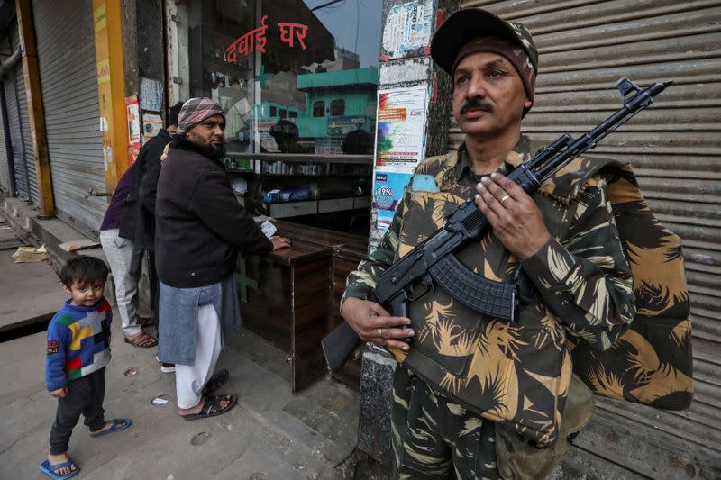 A paramilitary soldier stands guard outside a chemist shop at a riot affected area after clashes erupted between people demonstrating for and against a new citizenship law in New Delhi