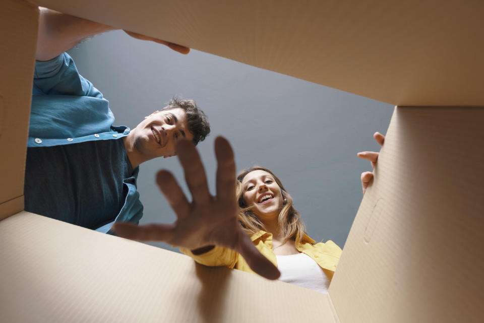 Happy couple opening a cardboard box and looking inside, they are smiling and cheerful