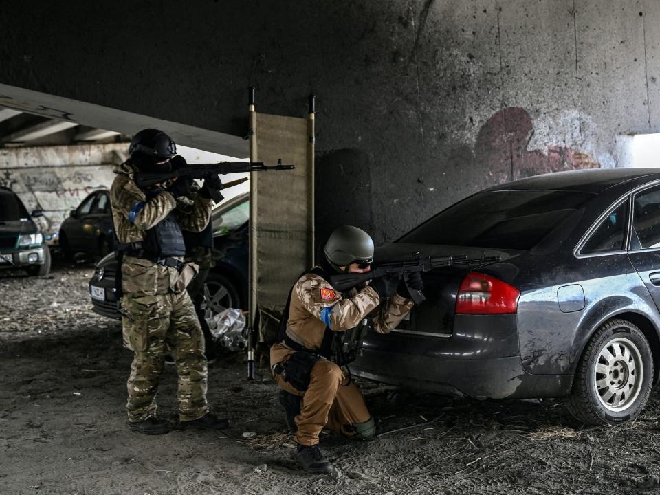 Ukrainian servicemen aim with their weapons at a moving car from underneath a destroyed bridge in the city of Irpin, northwest of Kyiv, on March 13, 2022.