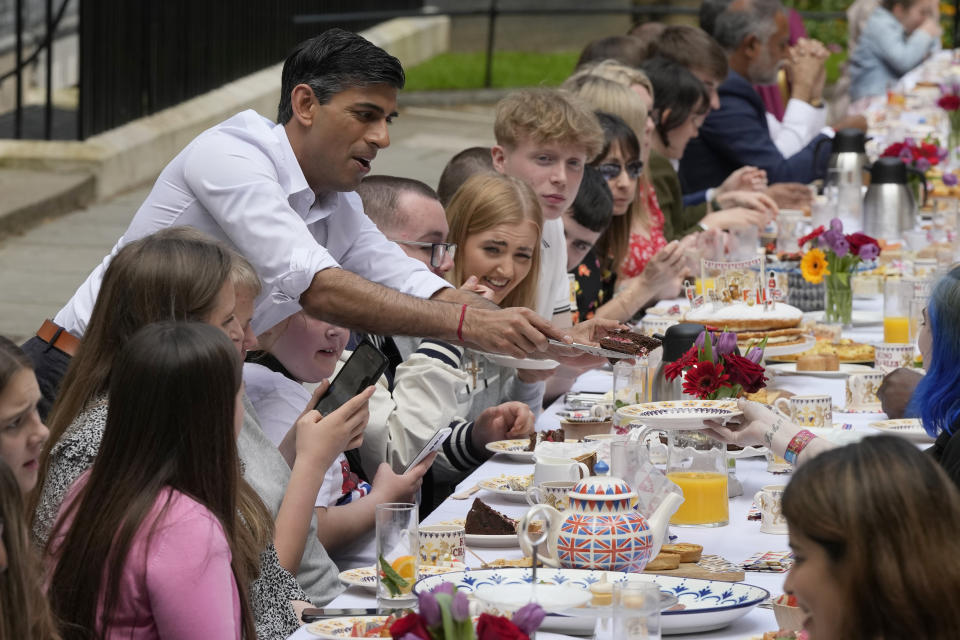 Prime Minister Rishi Sunak hands over a slice of cake to a guest as he attends the Big Lunch party at Downing Street in London Sunday, May 7, 2023. The Big Lunch is part of the weekend of celebrations for the Coronation of King Charles III. Guests at the big lunch include community heroes and Ukrainians displaced by the war, and youth groups. (AP Photo/Frank Augstein, Pool)