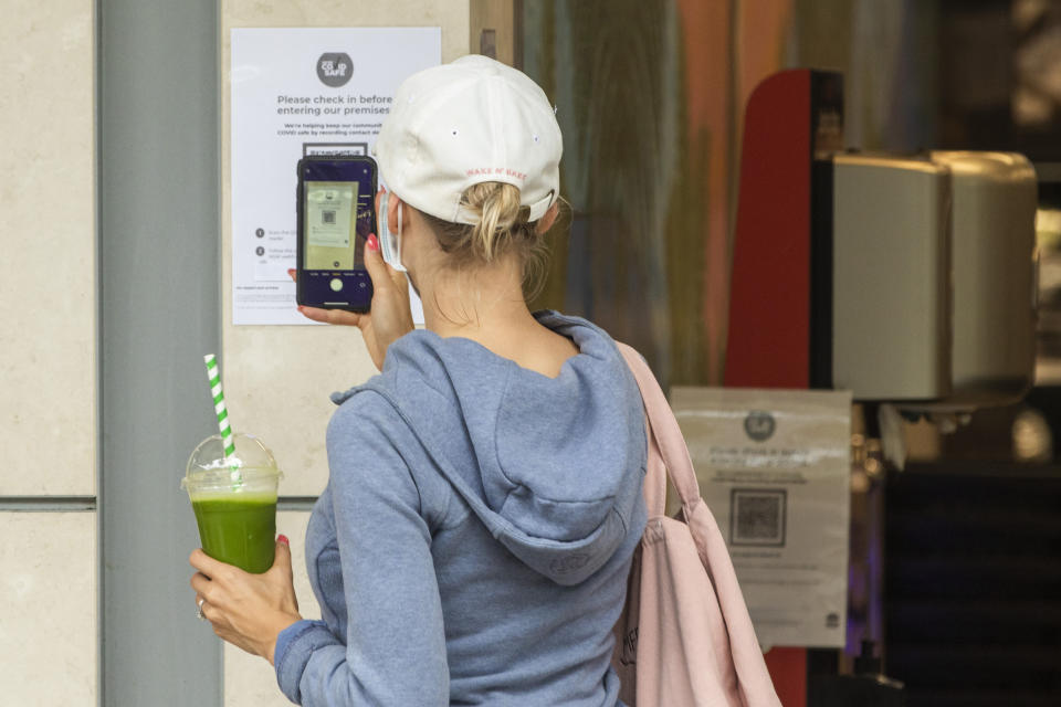 A woman holding a drink and wearing a mask scans a QR code on her phone. Source: Getty Images