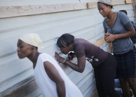 People peep through a hole in the wall while trying to catch a glimpse of the dead bodies of people who were killed when a carnival float hit power lines, at the morgue in Port-au-Prince February 17, 2015. REUTERS/Andres Martinez Casares