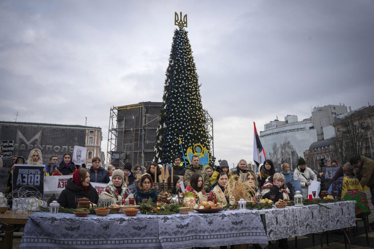 Relatives of soldiers from the Azov Regiment, who were captured by Russia in May after the fall of Mariupol, sit at the Christmas table in a flashmob action under the Christmas tree demanding to free the prisoners, in Kyiv, Ukraine, Saturday, Dec. 24, 2022. (AP Photo/Efrem Lukatsky)