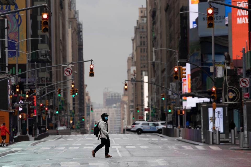 A man wearing a mask crosses the street in a quiet Times Square.