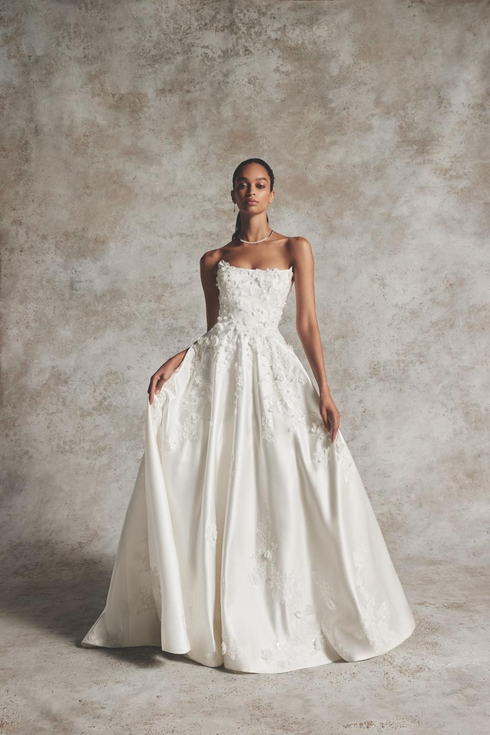 A woman in a wedding dress stands in front of a grey backdrop.