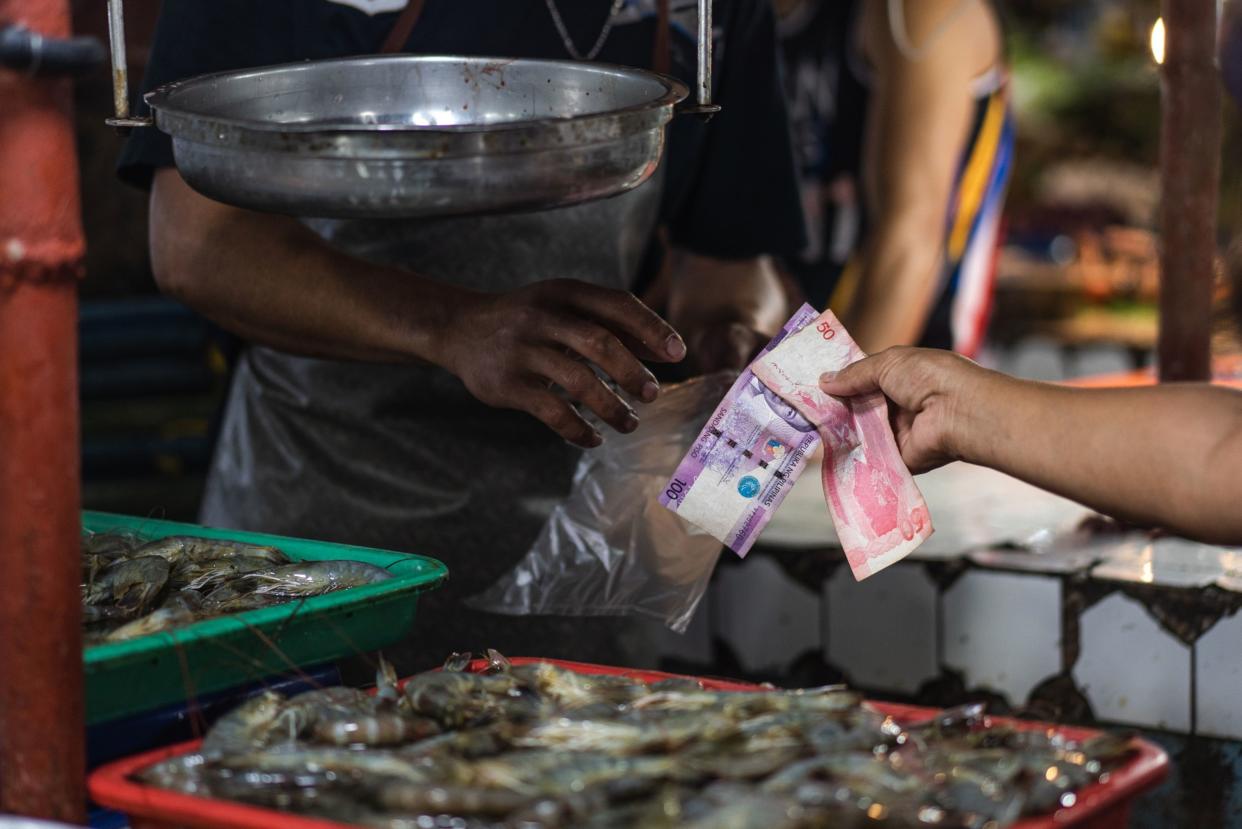A shopper hands Philippines' peso at a market in Mandaluyong. Photographer: Iya Forbes/Bloomberg