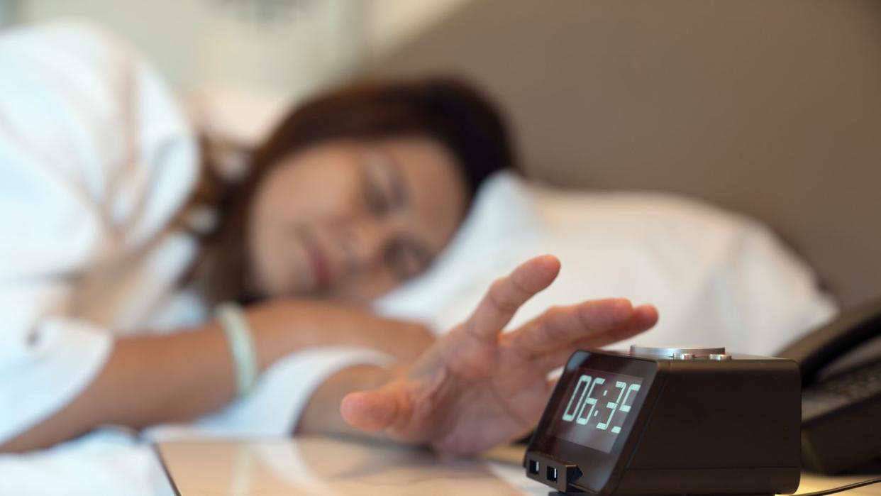 woman pressing the stop button on her alarm clock