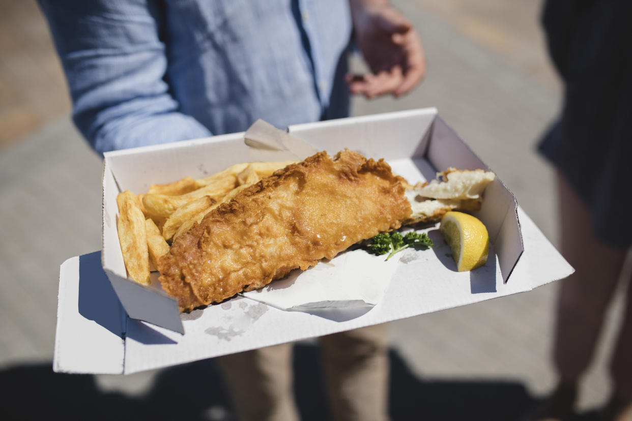 Person holding cardboard box with battered fish and chips, traditionally British, British food, takeaway food