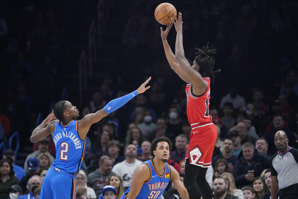 Chicago Bulls guard Ayo Dosunmu, right, shoots over Oklahoma City Thunder guard Shai Gilgeous-Alexander (2) and forward Jeremiah Robinson-Earl (50) in the first half of an NBA basketball game Monday, Jan. 24, 2022, in Oklahoma City. (AP Photo/Sue Ogrocki)