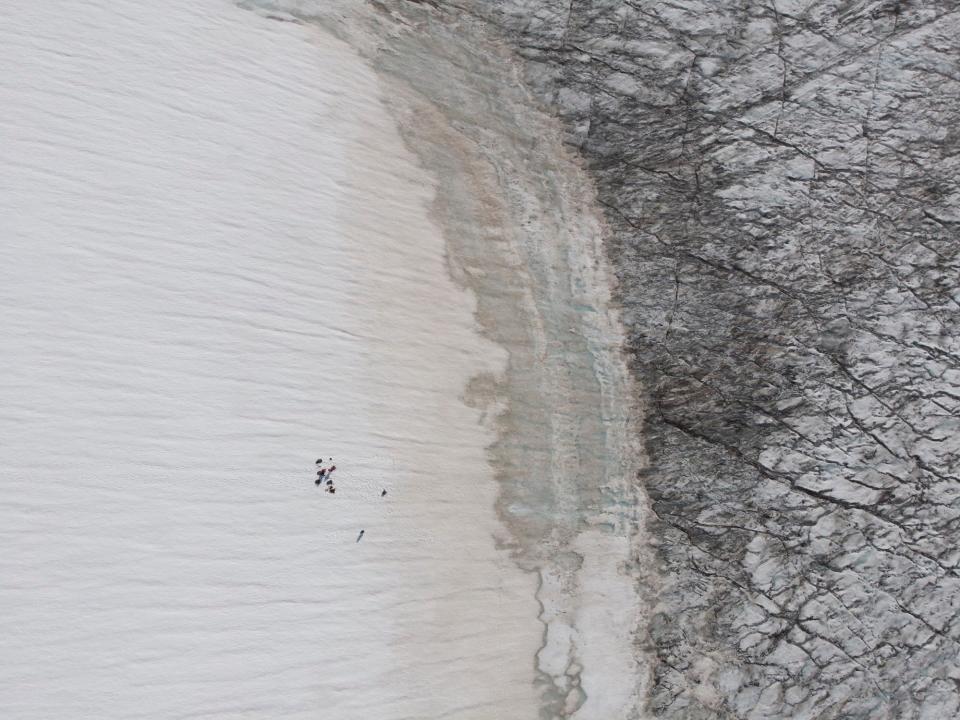 drone image shows people walking across white snow toward black cracked snow