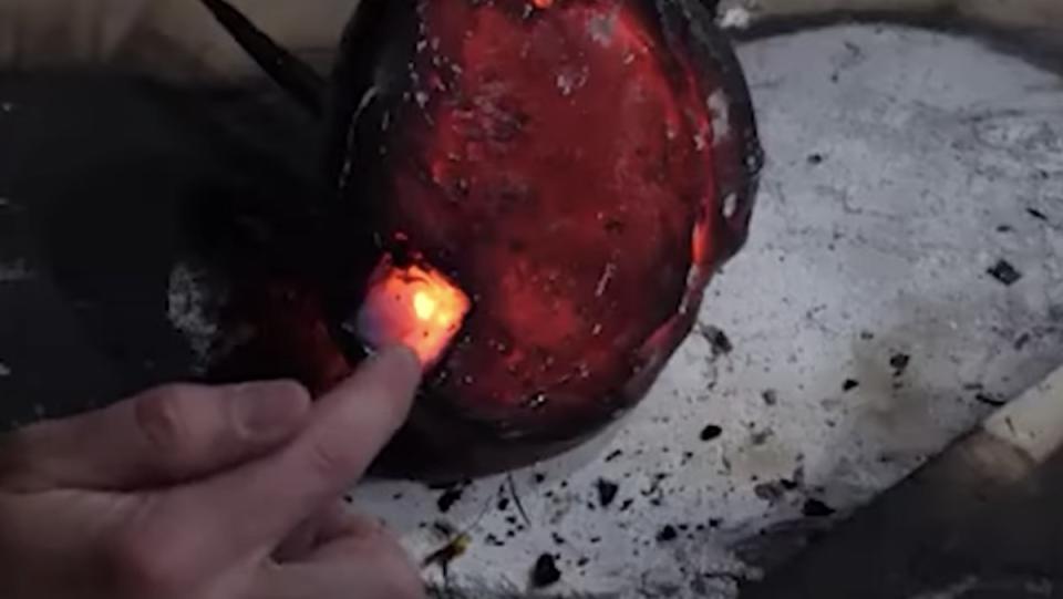 A finger touches a small square of aerogel lodged into a ball of glowing red magma