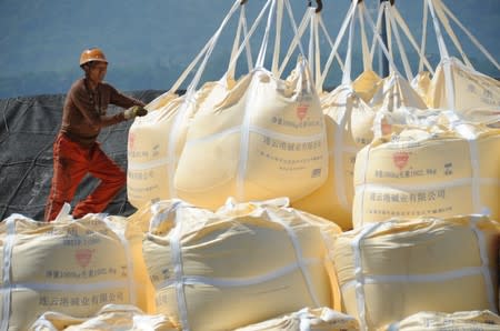 Worker helps a crane transporting sacks of soda ash for export at a port in Lianyungang, Jiangsu