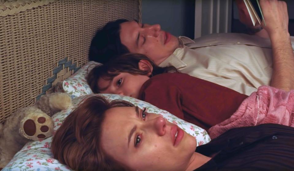 Adam Driver reading a book, Azhy Robertson putting his head on a pillow, Scarlett Johansson looking tearful as they lay in bed together