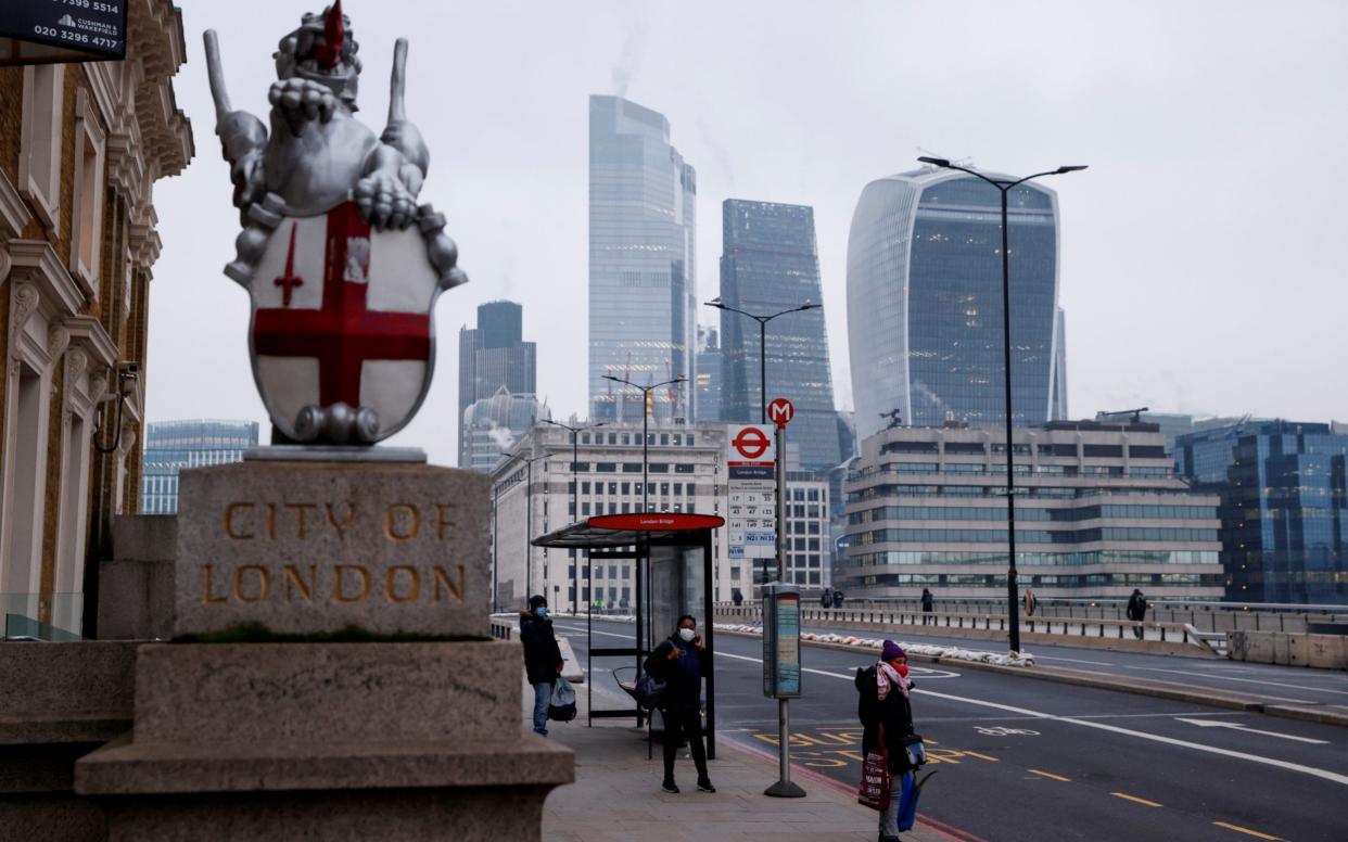 People wearing face masks wait at a bus stop on London Bridge, amid the outbreak of the coronavirus disease (COVID-19), with the City of London financial district in the background - JOHN SIBLEY /Reuters