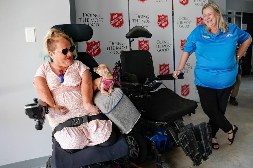 Angie Beer and her chihuahua Bella glance at each other in their new electric wheelchair as Salvation Army program manager Lisa Loren laughs at the Salvation Army in Naples on Wednesday, Feb. 15, 2023. 